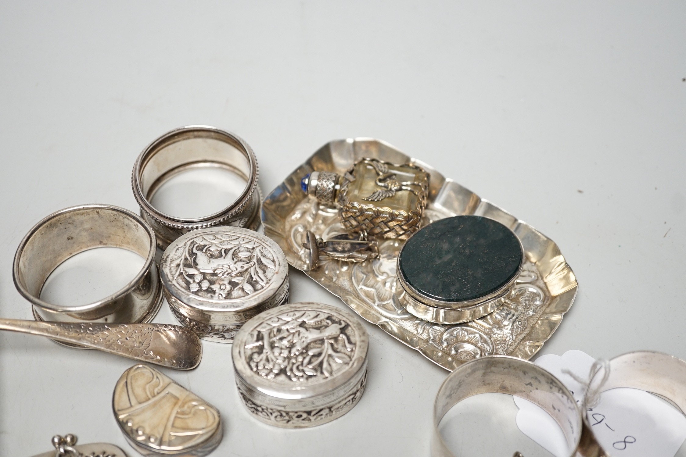 Sundry small silver including four assorted napkin rings, mounted bible, butter knife, pin tray, wine label etc. together with two white metal oval pill boxes, a moss agate mounted oval pill box and scent bottle.